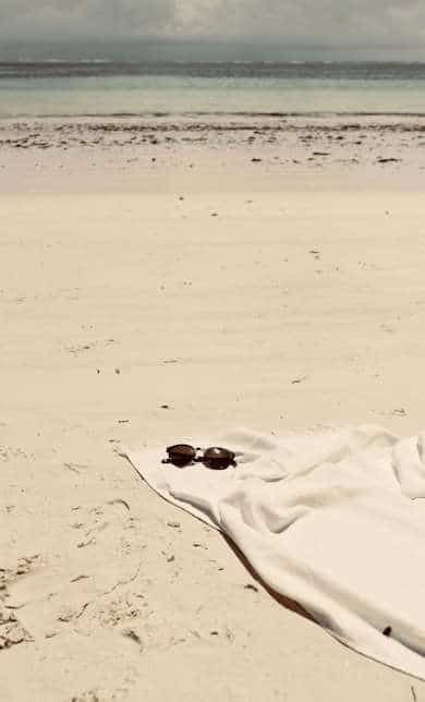 Extra long white beach towel on the beach with brown sunglasses