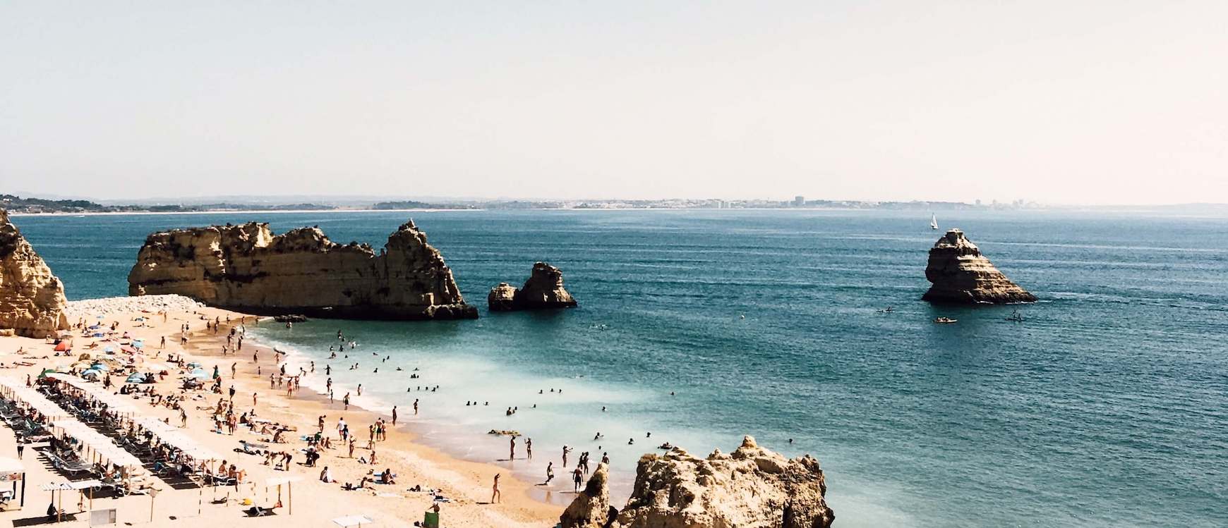 Crowded beach with blue water and cliffs