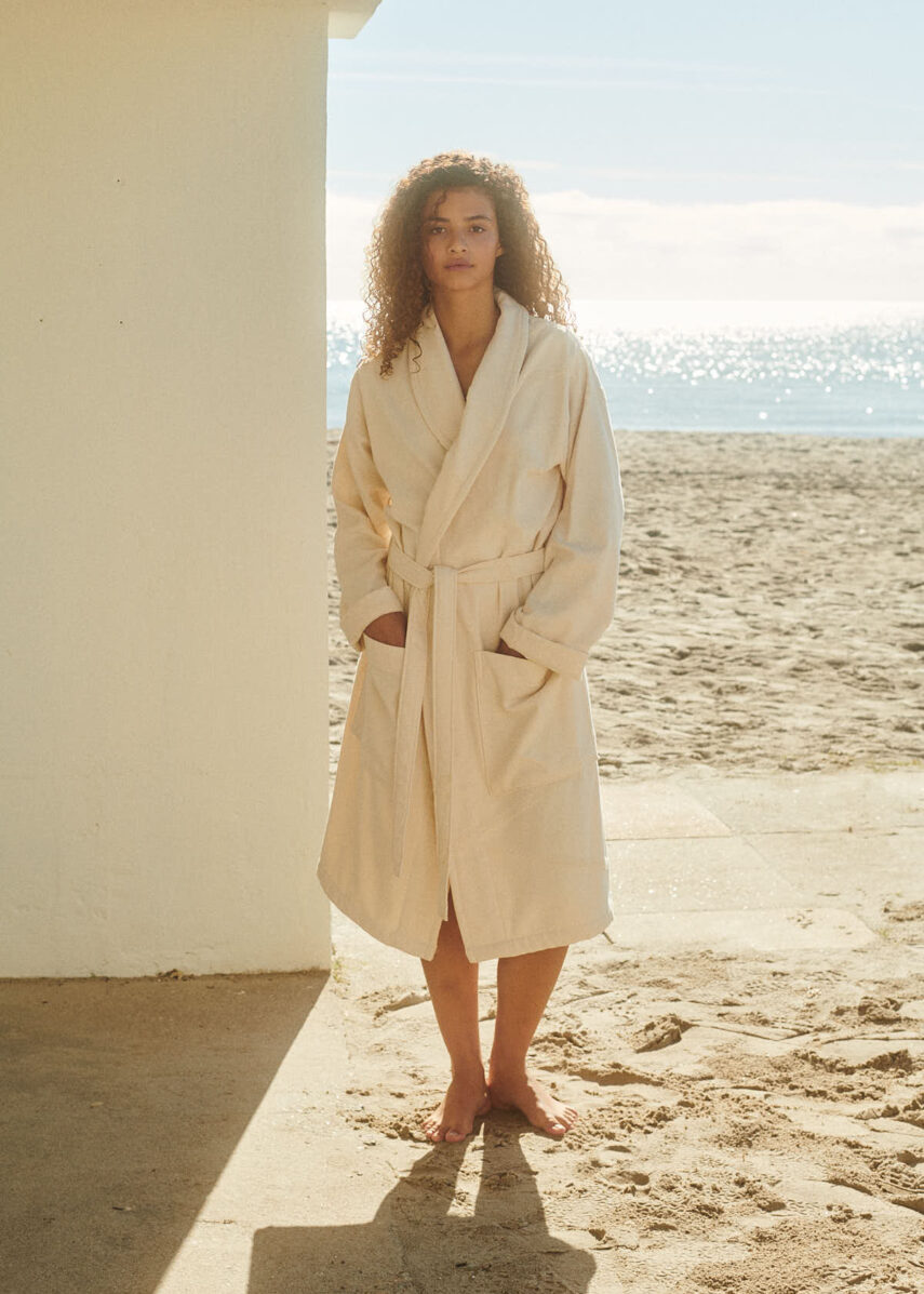 Marin bathrobe from WAY in SHell on a girl who is on the beach in bright sunlight. Organic cotton. recycled cottonl.