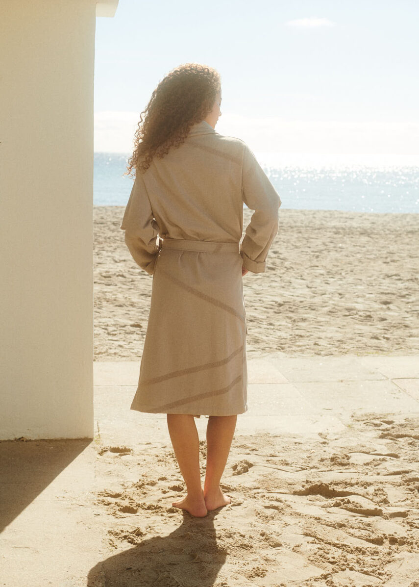 Girl at the beach from the behind wearing WAY Marin bathrobe in stone light grey