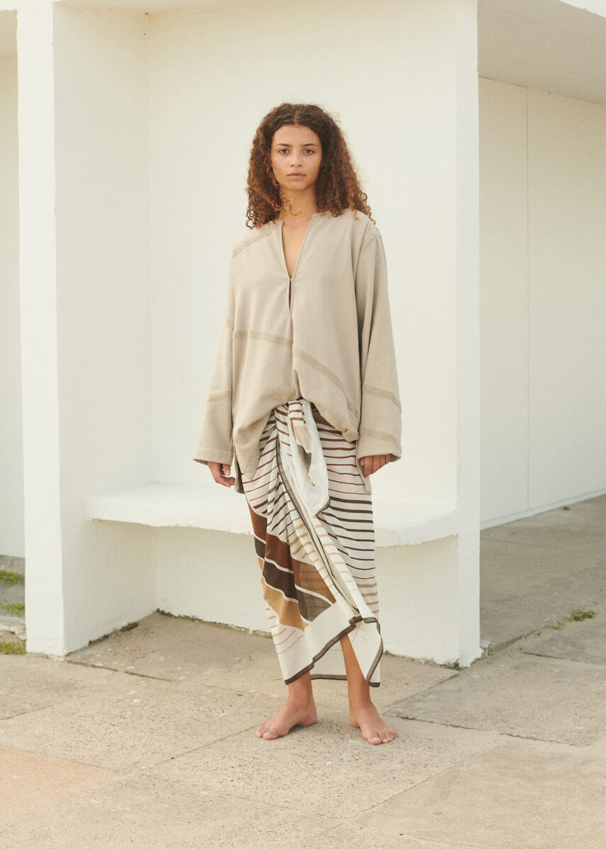 Girl at the beach wearing WAY Mala Kaftan in Stone and a sarong
