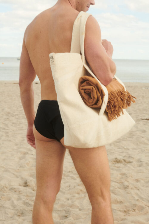 Man holding a big bossa beach bag from WAY with a brown beach towel in SAHARA colour from WAY