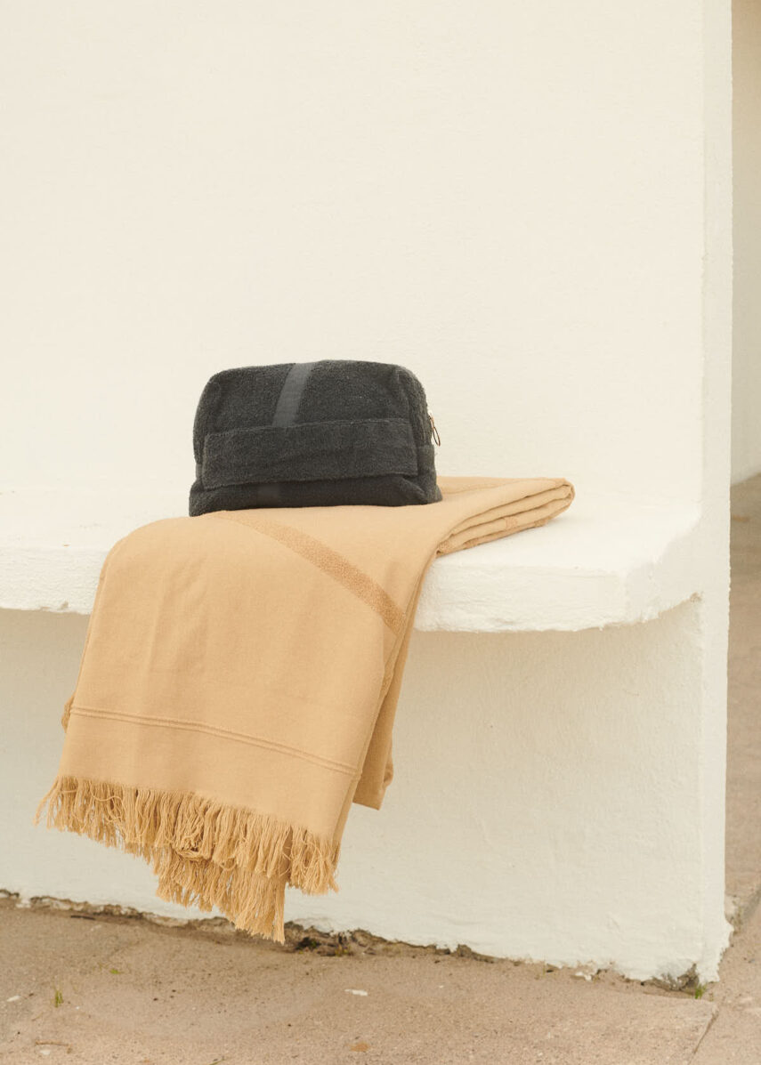 Amalfi Pouch from WAY in dark grey with a camel coloured beach towle on a white bench