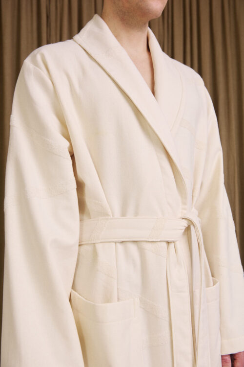 Close-up of WAY unisex Marin Bathrobe in cream white on male model in front of a curtain in a bungalow mansion