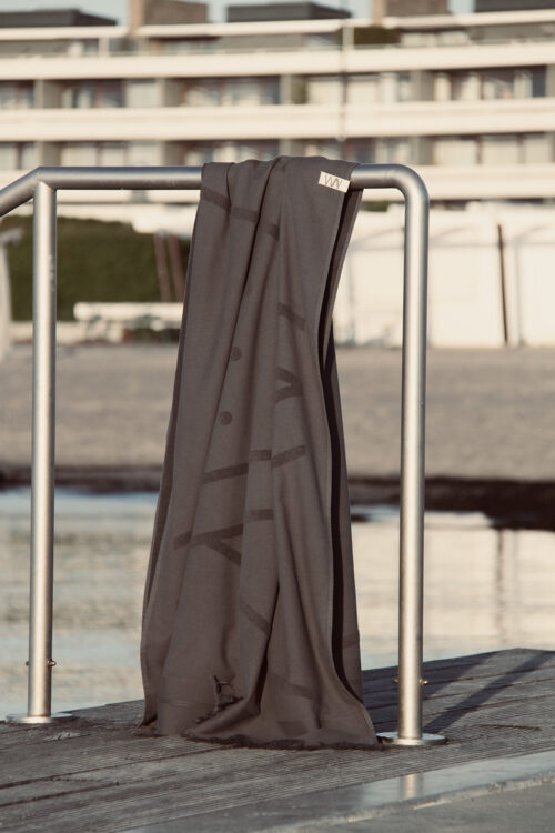 WAY beach towel in dark grey hanging on a pole by the beach with ocean view