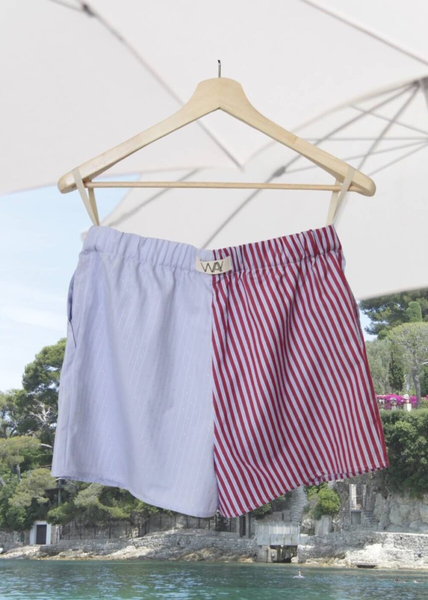 Upcycled blue striped SUN Shorts from WAY collaboration with Salvation Army with beach in back ground