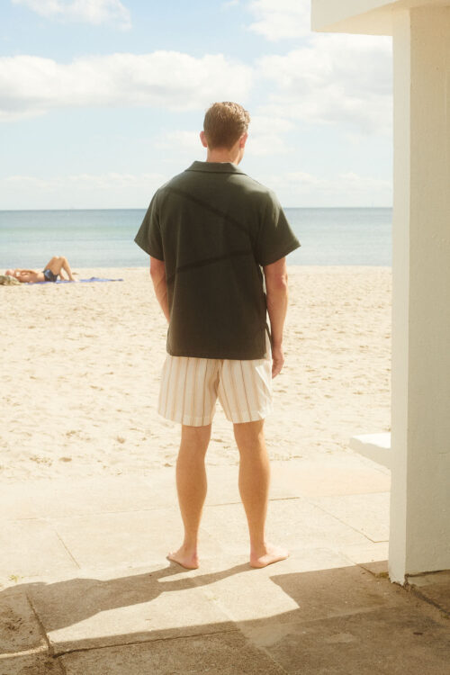 Saona shorts on male model at the beach from behind with a dark grey polo