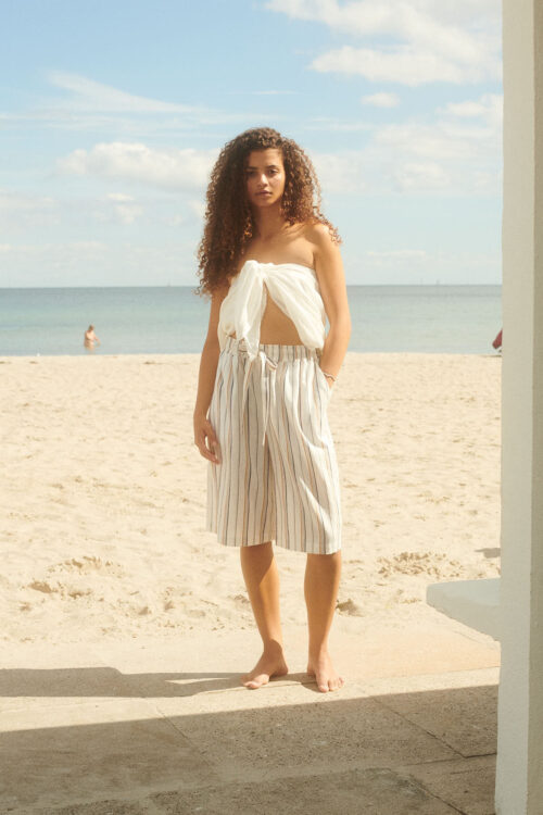 Female model wearing long board shorts in yellow stripes at the beach