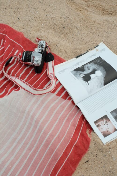 Red pareo in the sand with a vintage camera and open fashion magazine