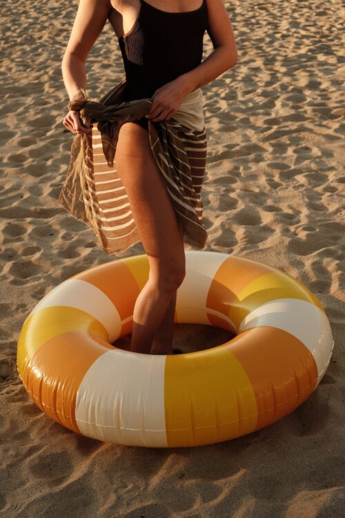 Girl at the beach tying a brown sarong and standing in a oragne pool float the beach