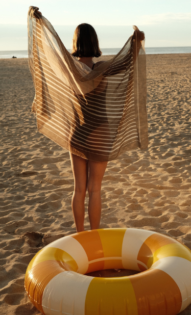 Girl on the beach holding up a sarong in front of a pool float